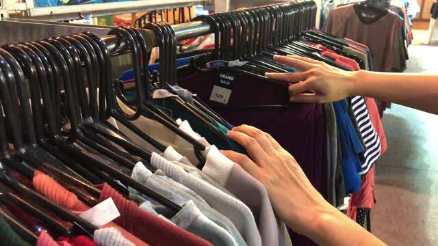 Close-up of female hands plucked a hanger with clothes. Woman's hands run across a rack of clothes. Dolly shot from the side. Woman's hand smoothing a colorful clothes. Close-up a hanger for clothing