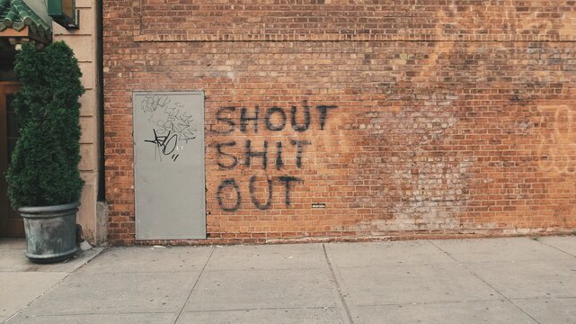 A city sidewalk with profanity graffiti on a brick wall