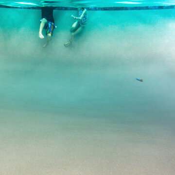 Two Kids Hang From the Edge of the Pool In the Deep End