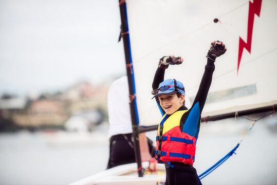 Boy about to go sailing raises arms in a cheer