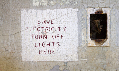 "Save Electricity, Turn Off Lights Here" sign painted on the wall next to the missing light switch