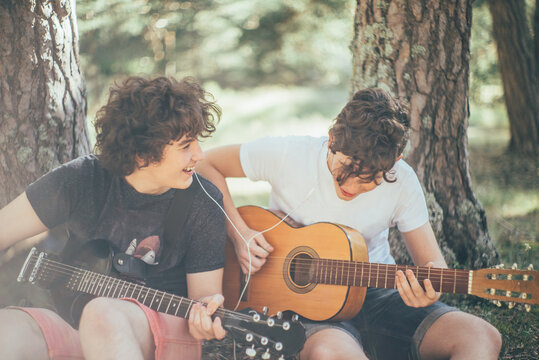 Two teenagers listening to music sharing their headphones while playing the guitar.