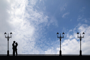 Silhouetted young lovers on a promenade set against a blue cloudy sky