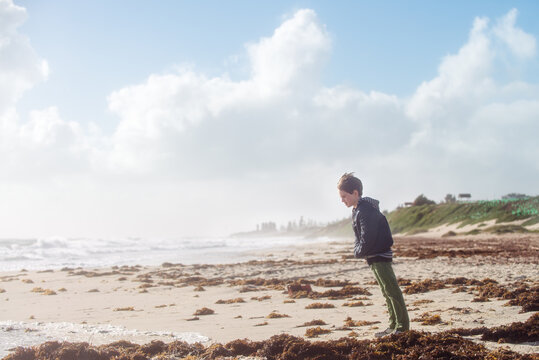Boy balances against the wind at the beach on a stormy and hazy day in winter