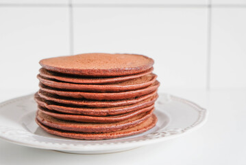 Freshly cooked chocolate pancakes stacked on white plate.