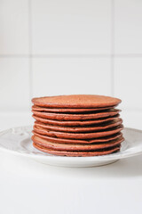 Freshly cooked chocolate pancakes stacked on white plate.