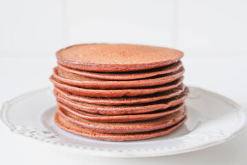 Freshly cooked chocolate pancakes stacked on white plate.