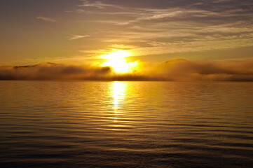 Fototapeta na wymiar 湖面に雲の漂う早朝の湖に昇る朝日