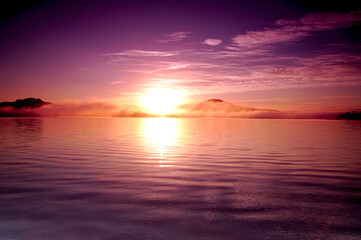 湖面に雲の漂う早朝の湖に昇る朝日