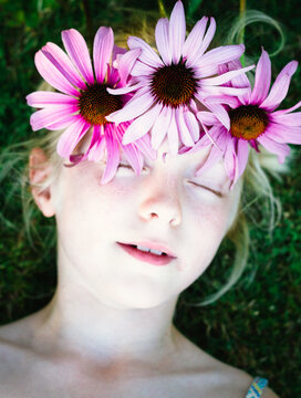 A little girl with a crown of pink flowers, her eyes closed.