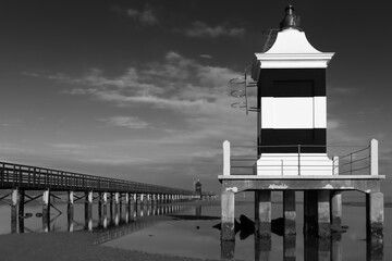 Black and white image of a pier and a lighthouse facing the Adriatic sea.  Lignano Sabbiadoro, Friuli Venezia Giulia, Italy.