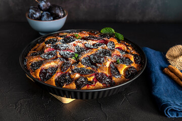Homemade plum pie with cinnamon. Fruit tart on black table.