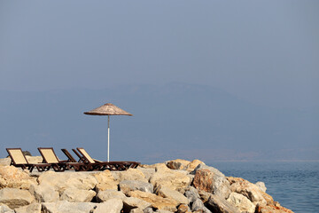 Empty deck chairs and sun umbrella on a stone beach on misty mountains background. Beach vacation...