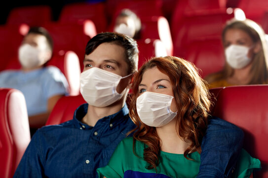 cinema, entertainment and pandemic concept - couple wearing face protective medical masks for protection from virus disease watching movie in theater