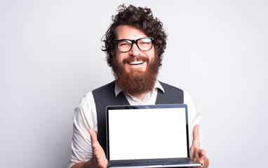 Joyful young man holding an open computer near a gray wall