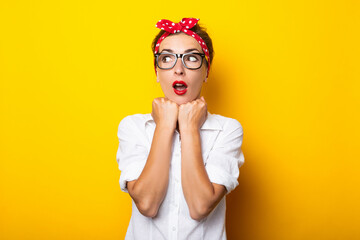 Young woman with a surprised face, wearing glasses and a headband on her head on a yellow background
