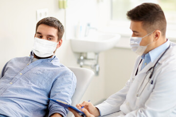 medicine, healthcare and pandemic concept - doctor wearing face protective medical mask for protection from virus disease with clipboard and young male patient at medical exam at hospital