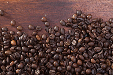 Picture of dark coffee beans on natural wooden background, no people