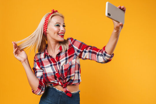 Image of happy pinup girl making smiling and taking selfie on cellphone