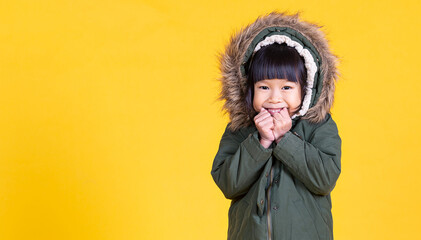 Portrait of young happy little asian girl wearing fur hooded winter coat sweater isolated on yellow...