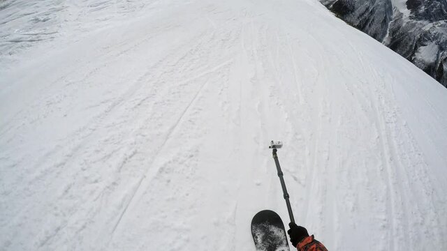 FPV snowboarder with action cam on monopod slide down prepared slope along track