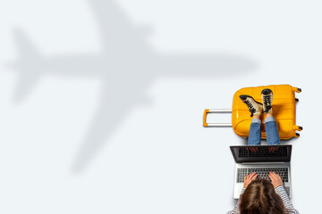 Young woman is sitting at the airport waiting for a flight with her feet on a suitcase and working on a laptop. Flat lay, top view