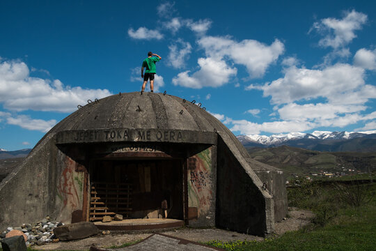 Young man standing on top of old bunker with snowy mountains in the background