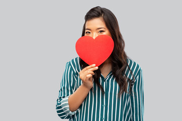 love, charity and valentines day concept - happy asian young woman covering face with red heart over grey background