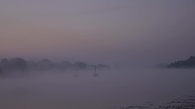 Two ancient authentic wooden boats on a lake or river in the morning during a foggy dawn. Footage shot with natural morning lighting in 4K background with constant focus