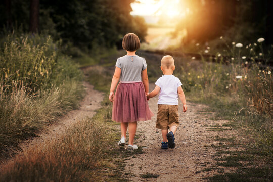 Two siblings walking in nature in the sunset. Brother and sister go on path and holding hands. Back view.