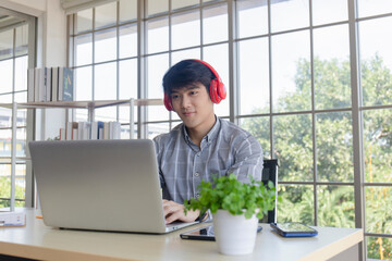 A young Asian businessman listens to music on a desk on a glass window balcony.