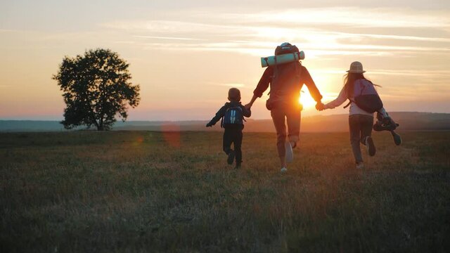Silhouettes of mother with two kids hiking on nature on sunset. Concept of friendly family.