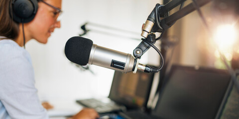 Microphone in a podcasting studio, host and the broadcasting equipment in the background