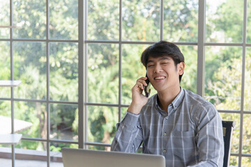 A young Asian businessman talking on the phone on a balcony window desk.
