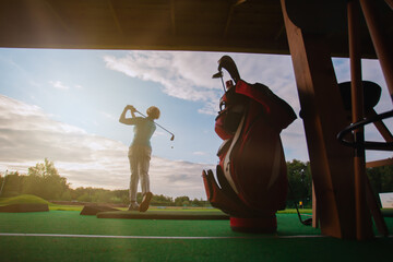 Kick the ball in golf against the backdrop of the setting sun with rays. Green golf course and...