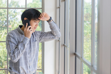 A young Asian businessman stands on the balcony of a window talking on the phone.
