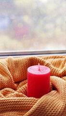 A red candle on the windowsill is wrapped in a winter scarf. Comfort, relaxation.