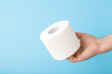 Young man hand holding soft, white toilet paper roll isolated on light blue background. Pastel color. Hygiene concept. Closeup.