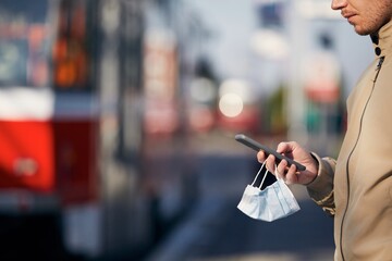 Man with face mask in hand using phone