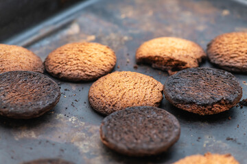 Burnt cookies. Burnt, burnt oatmeal cookies lie on a black baking sheet.