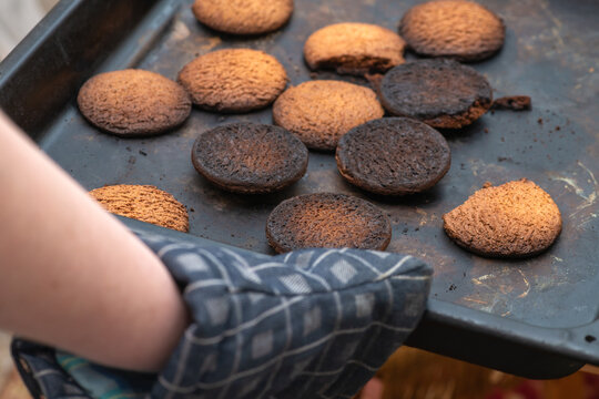 Burnt cookies. A hand in a oven glove, potholder picks up a black baking tray with burnt cookies