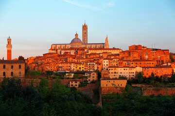 Obraz premium Sunset scenery of Siena, a beautiful medieval town on a hilltop in Tuscany Italy, with a view of architectural landmarks, Mangia Tower, Duomo Dome & Bell Tower bathed in warm, golden sunlight