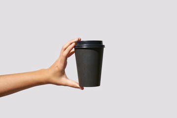 Girl hand hold coffee plastic cup. Grey background with copyspace. Female arm holding paper glass. To go, away. No ecology. Without shadows. Horizontal banner