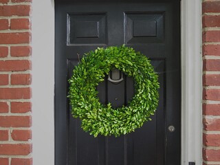 A green holly holiday wreath on a black door