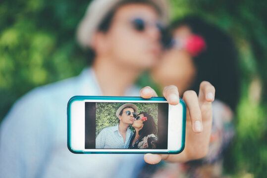 Young couple giving a kiss and making a picture with a cellphone.