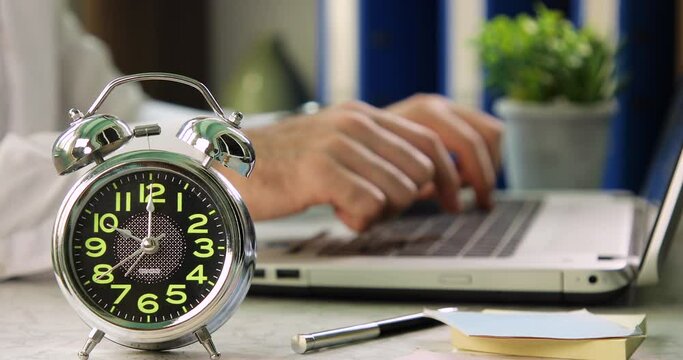 Man starting work on a laptop with a alarm clock. Work Time concept 10 am