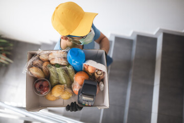 Delivery guy with protective mask holding box / bag with groceries and POS for contactless payment.