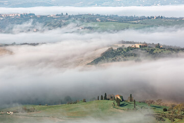 Naklejka na ściany i meble Beautiful scenery of idyllic Tuscany countryside on a foggy spring morning, with rolling hills veiled in morning fog and farmhouses perched on green hilltops in Pienza, Val d'Orcia, Tuscany, Italy