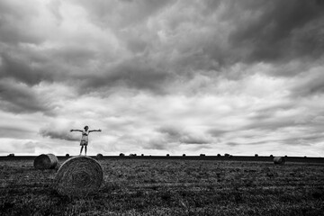 Girl Standing on Hay Bale With Dramatic Cloudy Sky on Farm