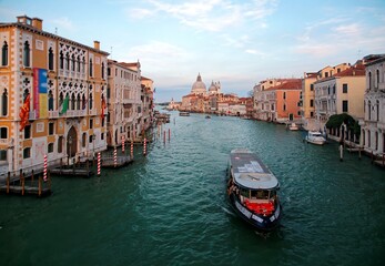 Romantic scenery of Venice bathed in dusk rosy light, with boats & ferries cruising on Grand Canal and landmark cathedral Basilica Santa Maria della Salute in background, an amazing city in Italy